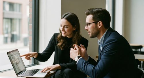 Empfehlungsmarketing Strategien für Freelancer in der Praxis. High resolution photography im Editorial Style: Zwei professionell gekleidete Personen (ein Mann, eine Frau, 30-40 Jahre alt) sitzen in einem modernen, minimalistischen Café. Die Frau zeigt auf ihrem Laptop-Bildschirm ein Projekt, während der Mann anerkennend nickt. Das Licht ist weich und natürlich, fällt durch ein großes Fenster. Die Szene wirkt authentisch und ungestellt (candid shot). Der Fokus liegt auf der positiven Interaktion der beiden. Shot on 35mm camera, Kodak Portra 400 style mit sichtbarem, aber feinem Filmkorn. Muted tones, depth of field mit leicht verschwommenem Hintergrund.